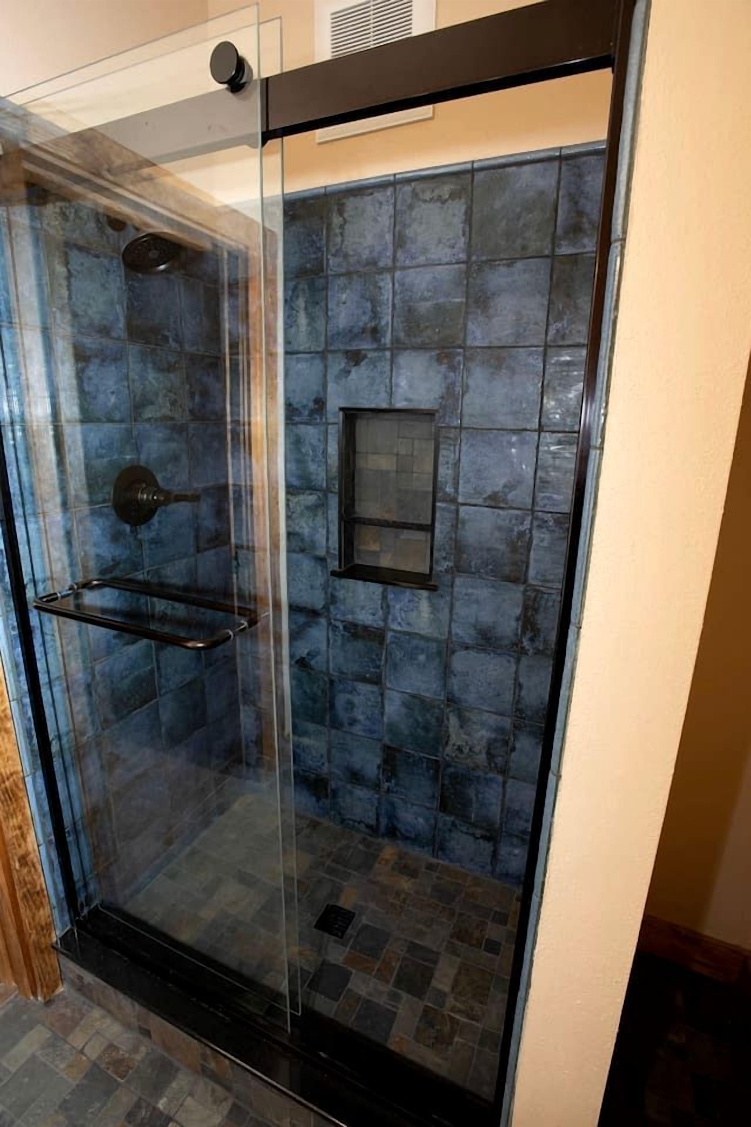 A glass-enclosed shower with a tiled wall, a shelf, and a vent.