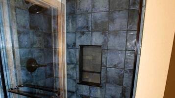A glass-enclosed shower with a tiled wall, a shelf, and a vent.