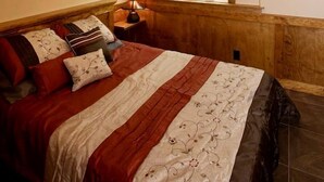 A bedroom with a sloped ceiling, a bed with multiple pillows, a bedside table with a lamp, and a window with a view of trees.