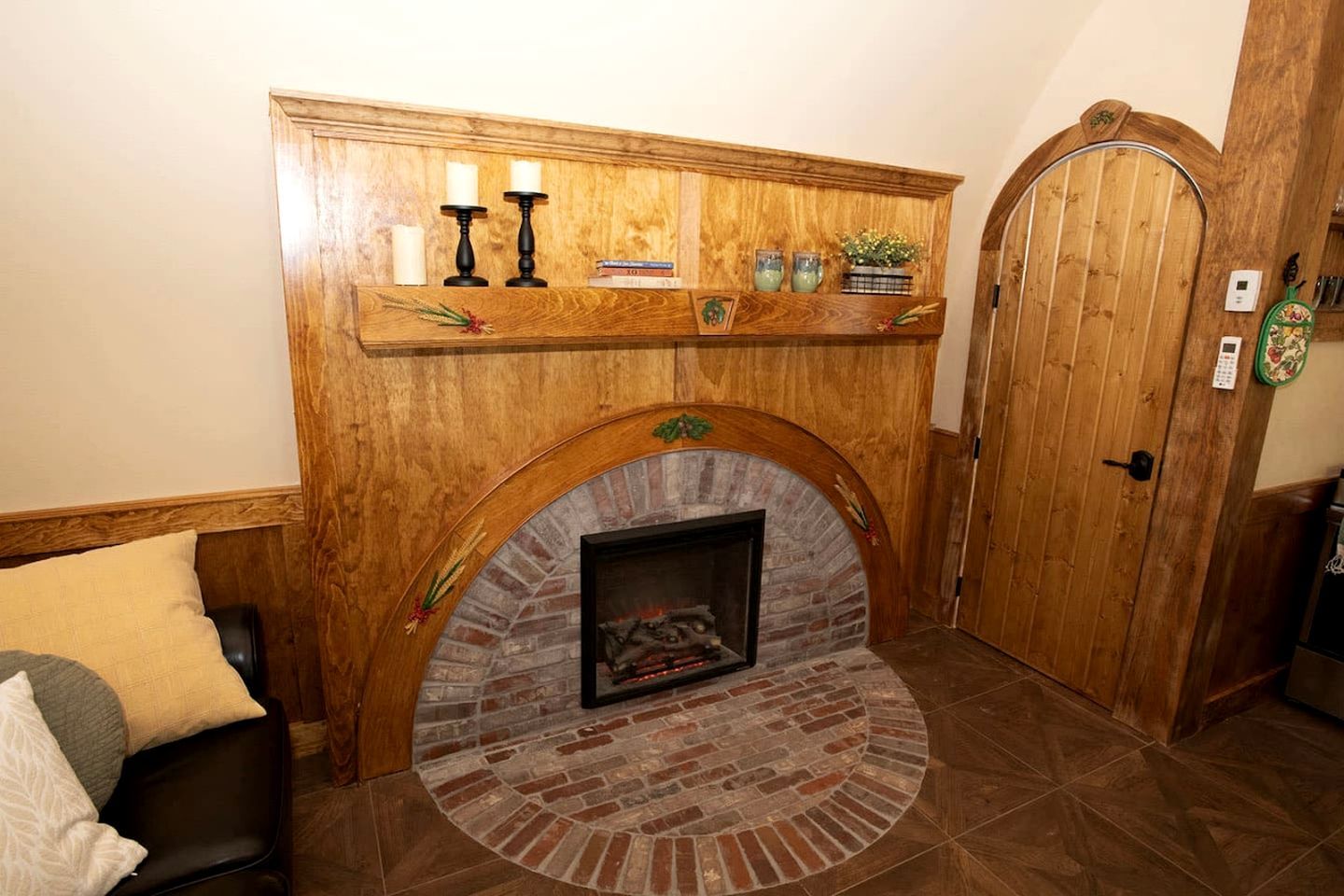 A fireplace with a brick surround, a wooden mantel with candles and books, and a wooden door with a keypad lock.