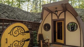 A small, rustic cabin with a wooden door, a circular window, and a bench outside.