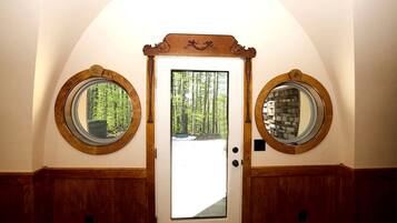A door with two round mirrors on either side, a central glass panel, and a view of a forest through the glass.