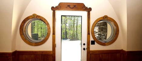 A door with two round mirrors on either side, a central glass panel, and a view of a forest through the glass.