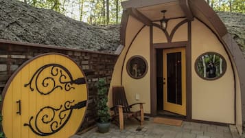 A small, rustic cabin with a wooden door, a circular window, and a bench outside.