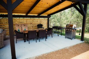 An outdoor patio with a wooden table and chairs, a grill, and a wooden wall with horizontal slats. - Idyllic Safari Tent Lovely for a Romantic Escape in Kentucky (Cadiz)