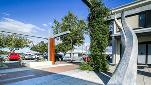 A modern building with a unique metal sculpture, a parking lot with several cars, and a clear blue sky. - Comfy 2-bedroom Apartment With a Clyde River View (Batemans Bay)
