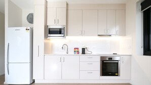 A modern kitchen with white cabinets, a white refrigerator, a microwave, a sink, and an oven. - Comfy 2-bedroom Apartment With a Clyde River View (Batemans Bay)