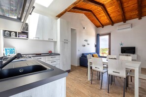 Eine moderne Küche mit Einbauherd, eine Essecke mit weißem Tisch und Stühlen sowie ein Wohnbereich mit blauem Sofa.