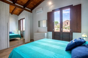 Ein Schlafzimmer mit Bett, Kommode, Spiegel und Fenster mit Blick auf ein Gebäude im Freien.