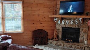 A cozy living room with a stone fireplace, a television mounted above it, and a leather sofa. - Honey Bear Hideway - Hot Tub - Close to Blue Ridge and Ellijay (Ellijay)
