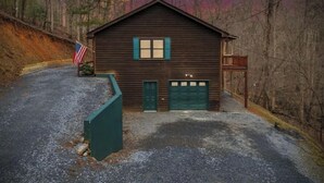 A wooden cabin with a green garage door, surrounded by a gravel driveway and a wooden fence. - Honey Bear Hideway - Hot Tub - Close to Blue Ridge and Ellijay (Ellijay)