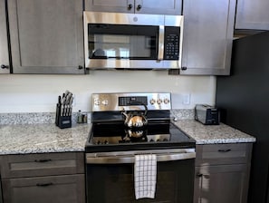 A kitchen with a stainless steel microwave, stove, and toaster, along with a kettle and knife block.