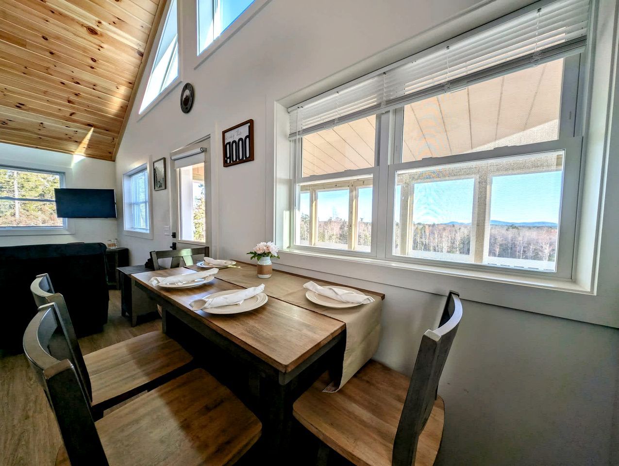 A dining area with a wooden table, chairs, and a view of the outdoors through large windows.