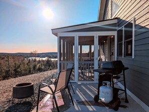 A covered outdoor area with a grill and propane tank, a chair, and a tire.