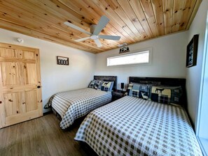A room with two beds, a ceiling fan, a wooden door, and a window.