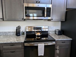 A kitchen with a stainless steel microwave, stove, and toaster, along with a kettle and knife block. - Peaceful Lakeside Cottage with Fire Pit & Screened Porch near Flanders Pond in Sullivan, Maine (Sullivan)