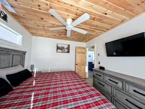 A bedroom with a bed, a ceiling fan, a TV, and a dresser. - Peaceful Lakeside Cottage with Fire Pit & Screened Porch near Flanders Pond in Sullivan, Maine (Sullivan)
