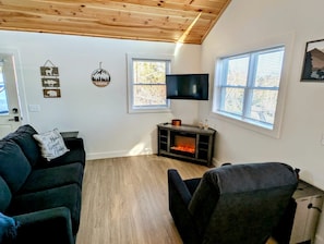 A living room with a fireplace, two sofas, a TV, and a window with blinds.