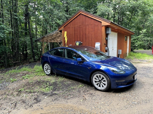 A blue car parked in front of a wooden building with a door labeled 'MAIL' and a lightning bolt sign.