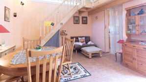 Een loft-achtige kamer met een houten wenteltrap, een eethoek met tafel en stoelen, een bank en een kast.