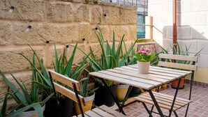 Een terras met een houten tafel en stoelen, omgeven door potplanten en een stenen muur.