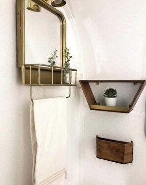 A bathroom with a towel rack, a mirror with a plant, and a small wooden box.