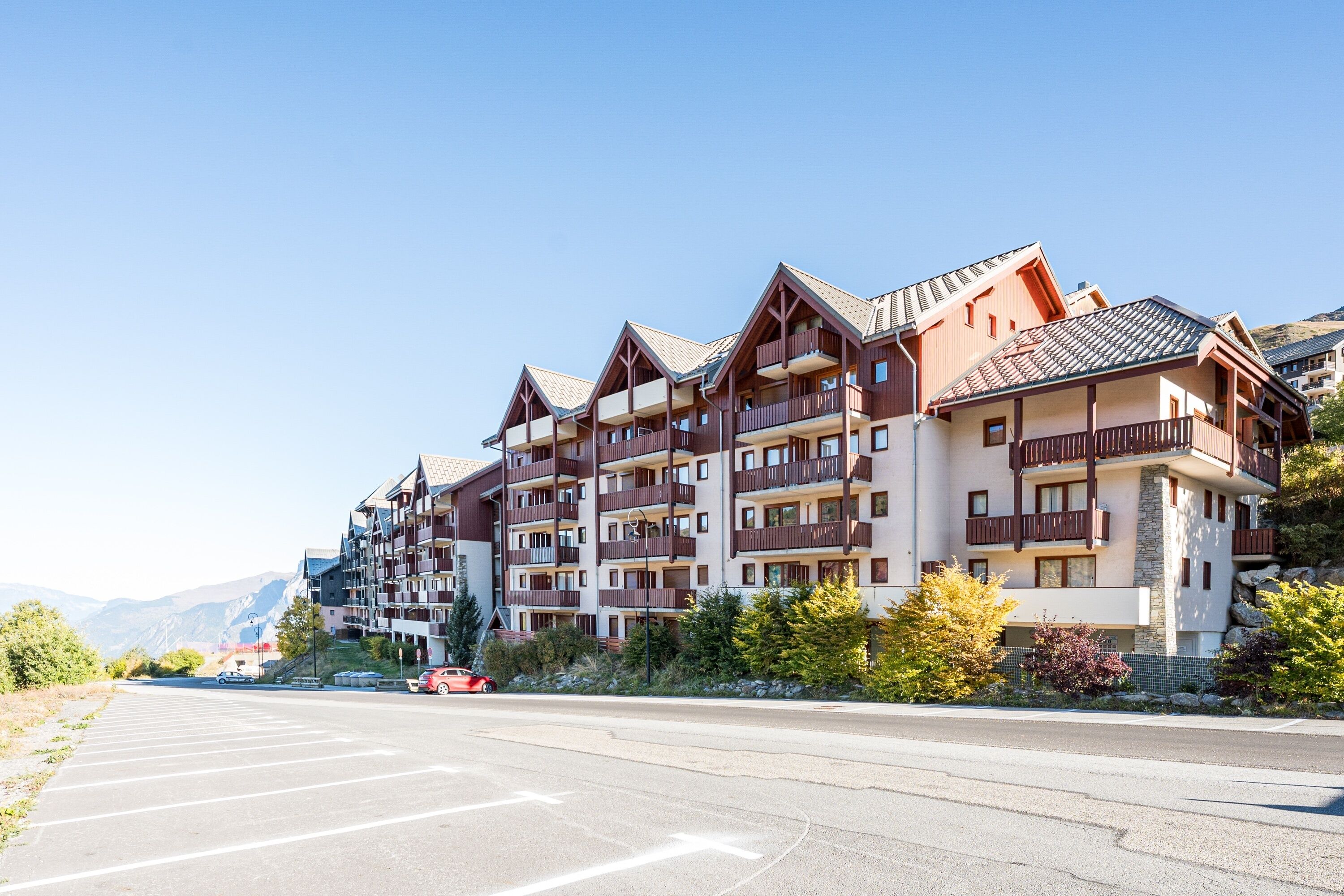 A multi-story hotel with balconies, a parking lot, and mountains in the background.