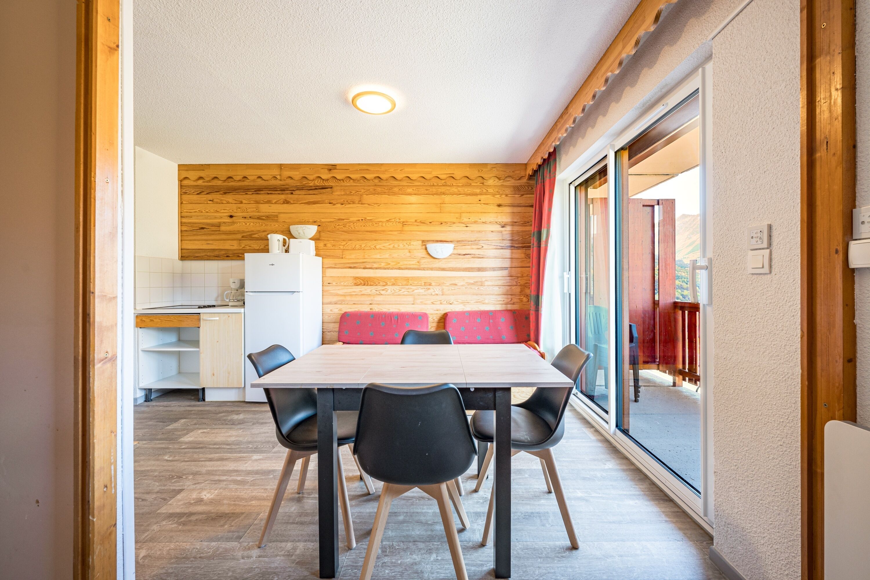 A dining area with a wooden wall, a table with chairs, and a view of the outside.