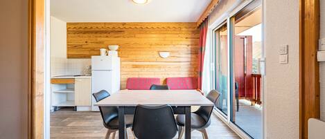 A dining area with a wooden wall, a table with chairs, and a view of the outside.