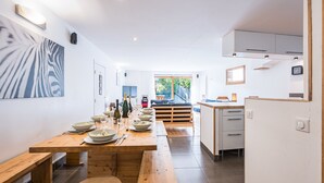 A modern kitchen with a wooden dining table set for a meal, a built-in oven, and a view of the garden. - La Grange - Chalet DDA La Combe (Saint Martin de Belleville)