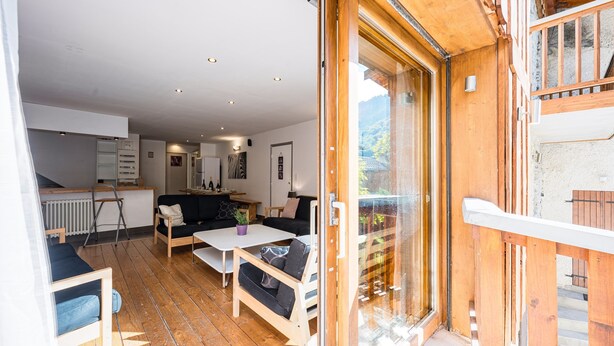 A cozy living area with a wooden floor, a sofa, a coffee table, and a sliding glass door leading to a balcony. - La Grange - Chalet DDA La Combe (Saint Martin de Belleville)