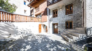 A stone building with wooden balconies, a cobblestone courtyard, and a wooden fence. - La Maison - Chalet DDA La Combe (Saint Martin de Belleville)