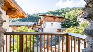 A wooden balcony with a stone wall, overlooking a village with traditional buildings and a mountainous backdrop. - La Maison - Chalet DDA La Combe (Saint Martin de Belleville)