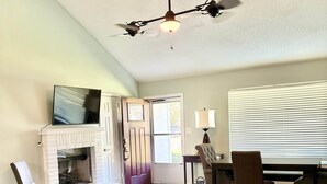 Ein Wohnzimmer mit Kamin, Deckenventilator, Fernseher und Essbereich mit Stühlen und Tisch.
