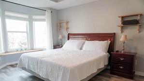 Ein ordentlich eingerichtetes Schlafzimmer mit einem großen Bett, einem Holz-Kopfteil, Nachttischen mit Lampen und einem Fenster mit Aussicht.