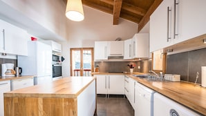 A modern kitchen with white cabinetry, a wooden island, and built-in appliances. - Le Grenier - Chalet DDA La Combe (Saint Martin de Belleville)
