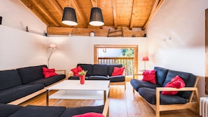 A cozy living room with wooden beams, black sofas with red cushions, a white coffee table, and pendant lights. - Le Grenier - Chalet DDA La Combe (Saint Martin de Belleville)
