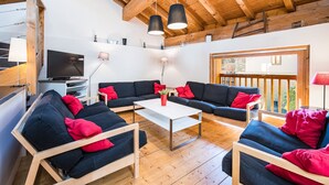 A modern living room with a wooden ceiling, black sofas with red cushions, a white coffee table, and a TV. - Le Grenier - Chalet DDA La Combe (Saint Martin de Belleville)