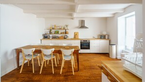 Una cocina moderna con armarios blancos, una mesa de comedor de madera con sillas y un amplio ventanal que proporciona luz natural.