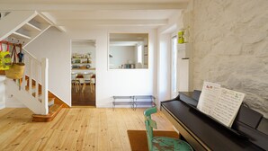 Amplia sala de estar con un piano, piso de madera, una escalera y una cocina al fondo.