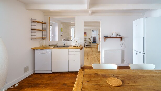 Una cocina moderna con armarios blancos, encimera de madera y comedor con mesa y sillas de madera.
