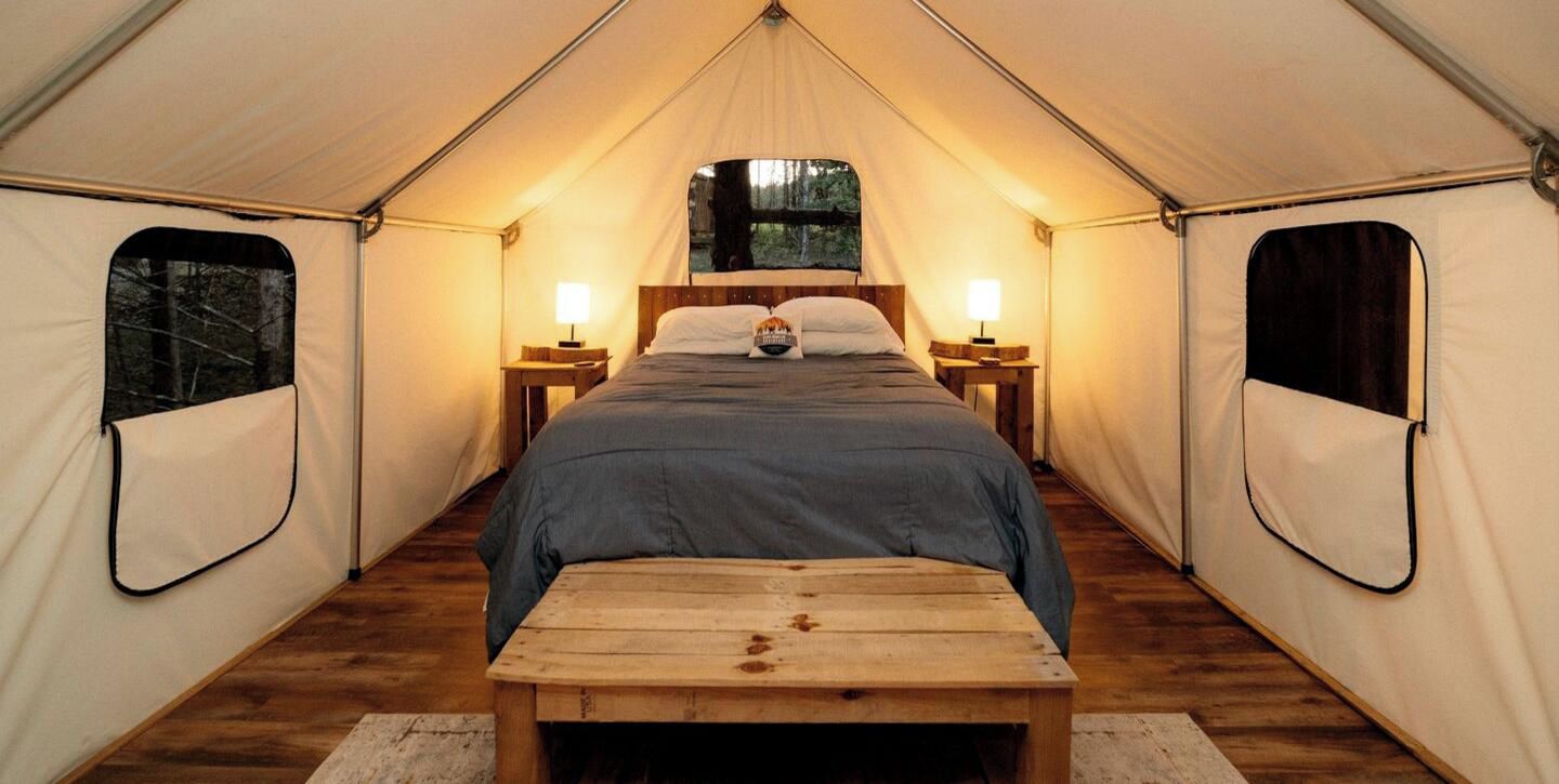 A tent with a single bed, two bedside tables, and a bench.