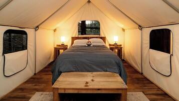A tent with a single bed, two bedside tables, and a bench.