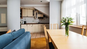 A modern kitchen with white cabinets, a wooden dining table, and a blue sofa. - Native Apartments Warszauera 3 (Kraków)