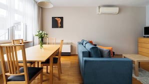 A modern living room with a wooden dining table, blue sofa, and a TV stand. - Native Apartments Warszauera 3 (Kraków)