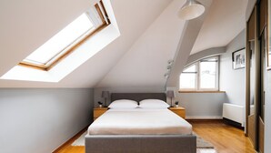A bedroom with a skylight, a bed, bedside lamps, and a view of the outside. - Native Apartments Warszauera 3 (Kraków)