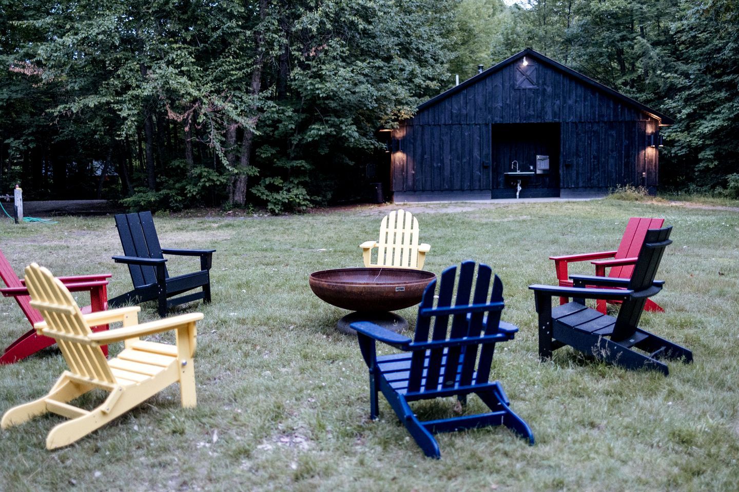 Ein rustikaler Außenbereich mit Adirondack-Stühlen und einer Feuerstelle, umgeben von einer Holzhütte.