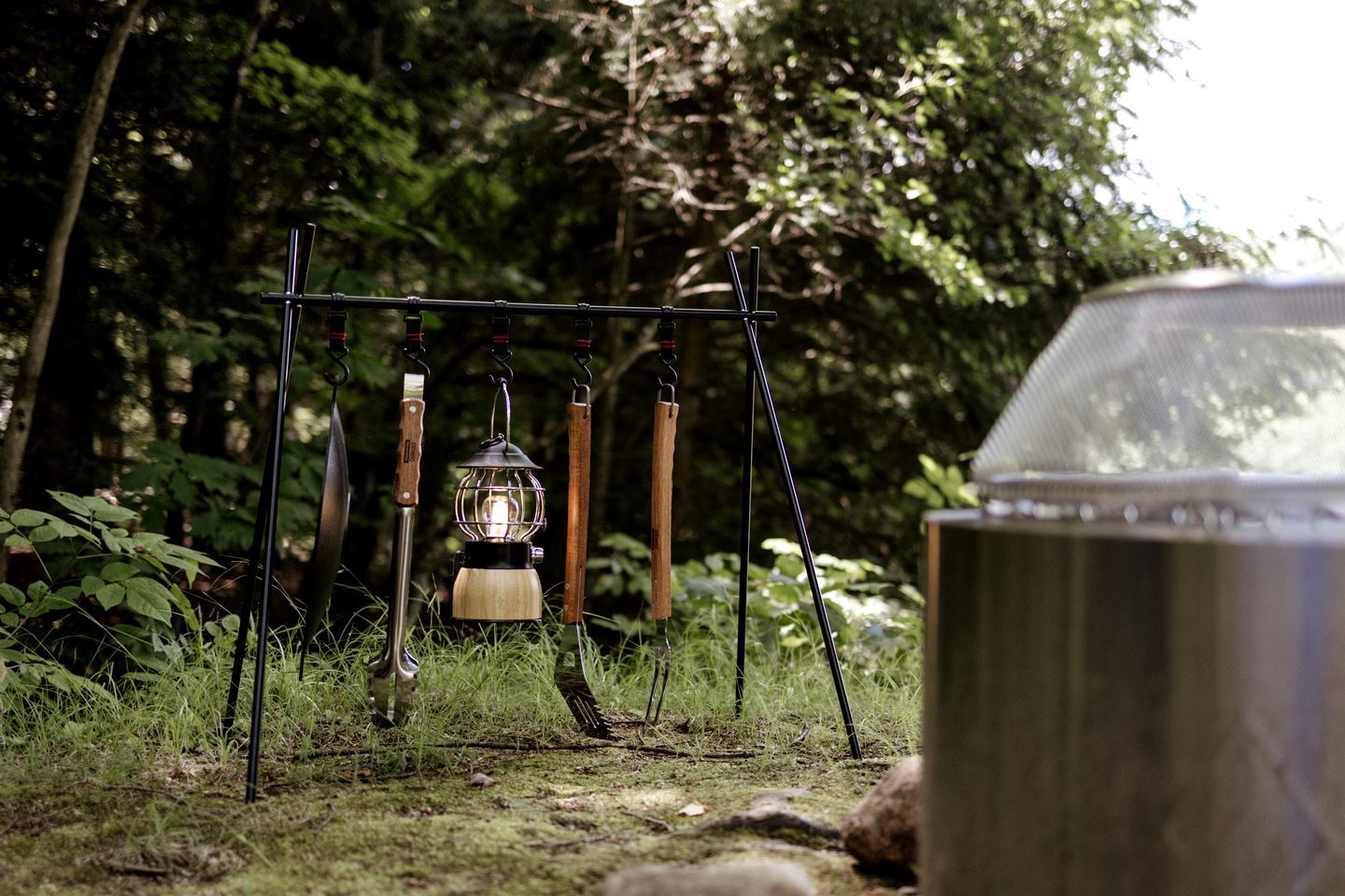A metal lantern hanging from a metal frame in a forested area.