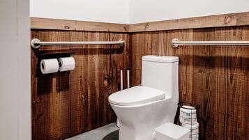 A small, compact bathroom with a wooden wall, a white toilet, and two rolls of toilet paper on a rack.