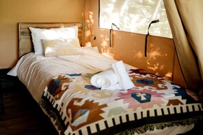 A bed with a patterned bedspread, pillows, and a rolled towel.